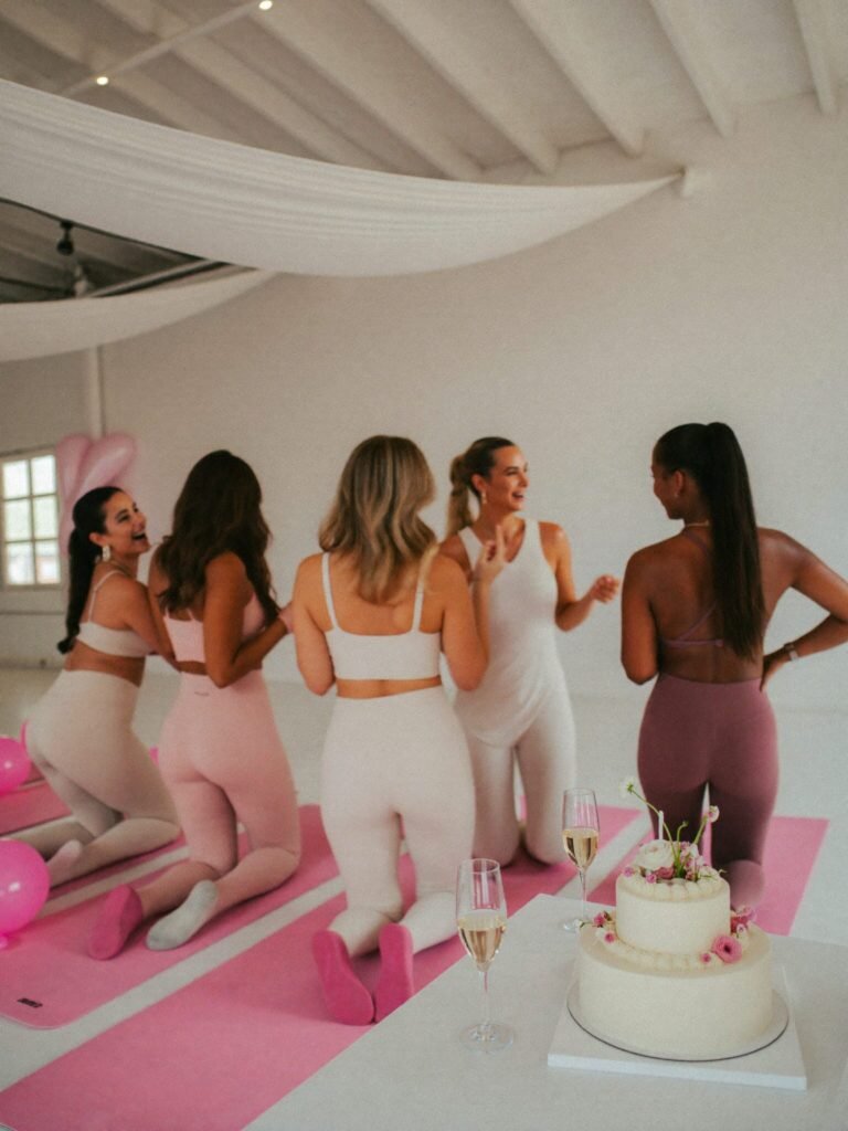 A bachelorette Pilates celebration with champagne, a white cake and pink balloons in a white studio
