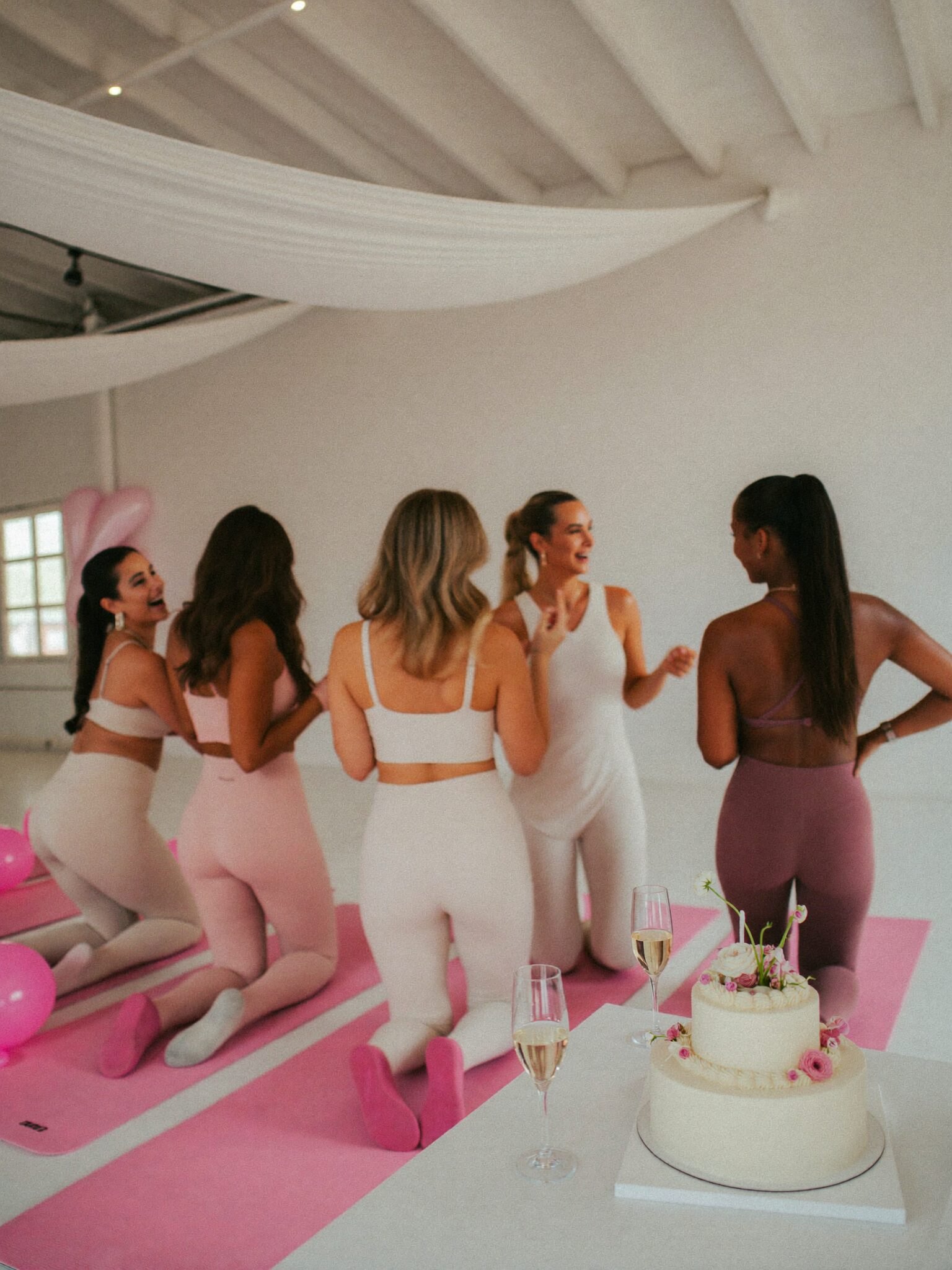A bachelorette Pilates celebration with champagne, a white cake and pink balloons in a white studio